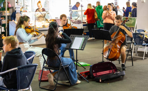 Four young musicians perform as a string quartet inside the Adelaide Showground Farmers’ Market, surrounded by marketgoers enjoying the music.