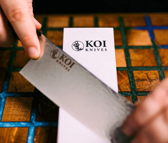 Hands sharpening a KOI knife on a whetstone during a demonstration.