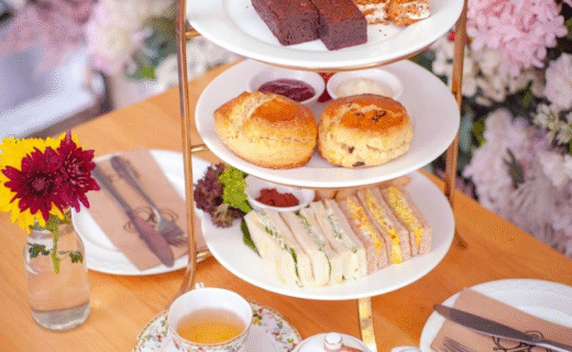 A beautifully styled high tea setting with a three-tier platter of sandwiches, scones, and cakes, served alongside a teapot and cup of tea at the Adelaide Showground Farmers’ Market.