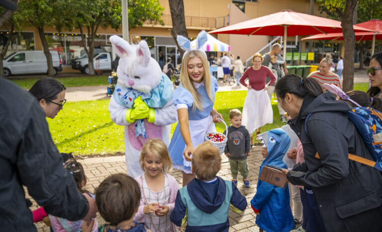 Children gathering around the Easter Bunny and a costumed helper handing out chocolate treats at the Adelaide Showground Farmers’ Market.
