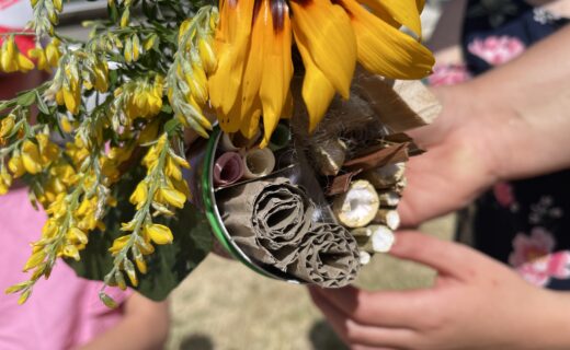 Child holding a handmade bee hotel made from a recycled tin can filled with natural materials and yellow flowers.