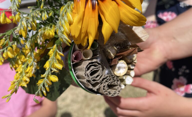 Child holding a handmade bee hotel made from a recycled tin can filled with natural materials and yellow flowers.