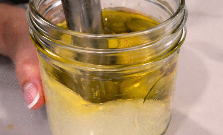 Immersion blender mixing fresh mayonnaise in a glass jar, showing oil and egg emulsifying during a kitchen demonstration.