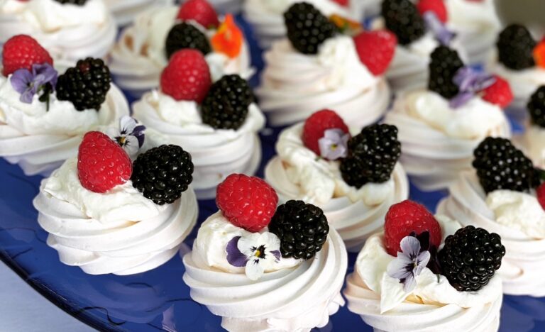 Mini pavlovas topped with whipped cream, fresh raspberries, blackberries and edible flowers on a blue platter at the Adelaide Showground Farmers’ Market.