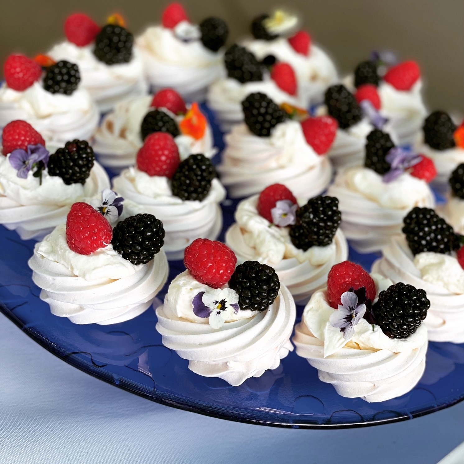 Mini pavlovas topped with whipped cream, fresh raspberries, blackberries and edible flowers on a blue platter at the Adelaide Showground Farmers’ Market.