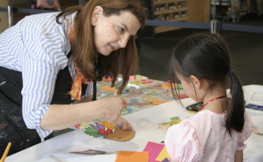 Art facilitator helping a child paint a portrait during a Kids Corner creative workshop inside the market pavilion.