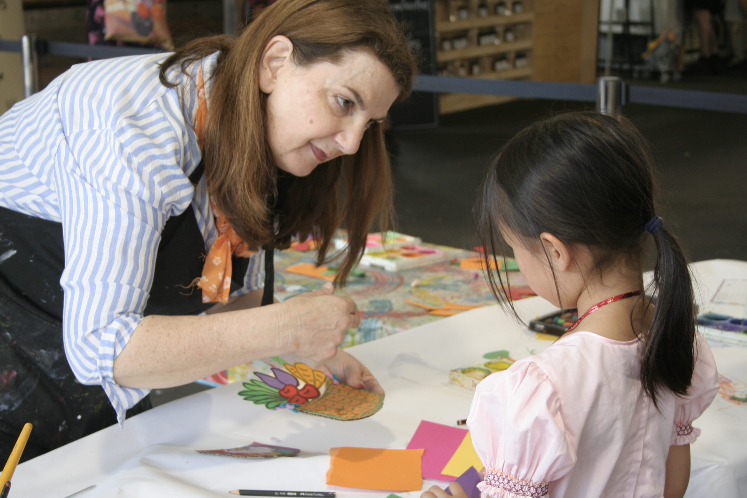 Art facilitator helping a child paint a portrait during a Kids Corner creative workshop inside the market pavilion.