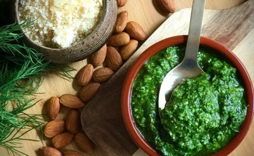 Bowl of fresh green pesto with almonds, grated cheese and herbs on a wooden board.
