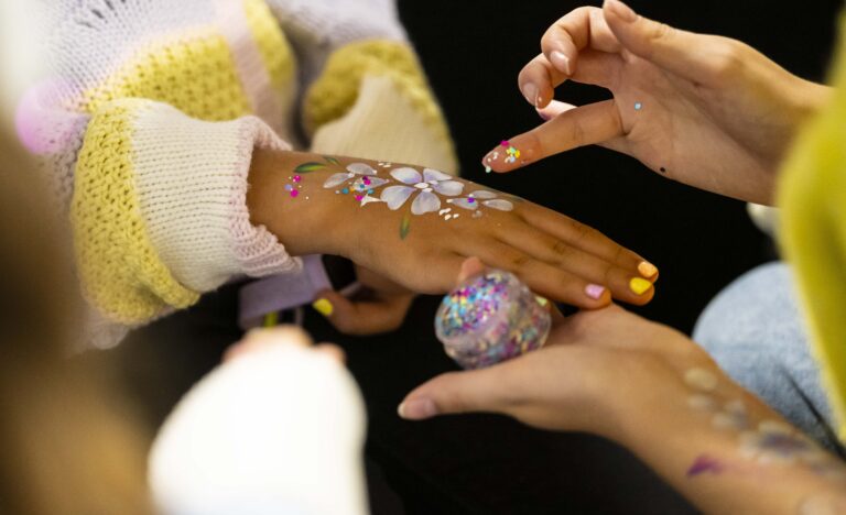 A child receives a colourful floral face painting design on their hand from Sparkles Face Painting during a family-friendly market morning at Adelaide Showground Farmers' Market.