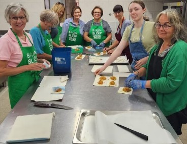 A group of Food on the Table volunteers work together in a commercial kitchen preparing and packaging meals for South Australians experiencing food insecurity.