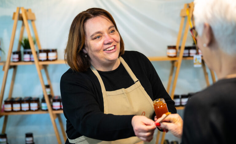 A Fiaje Jams stallholder offers a sample of handmade South Australian jam to a market visitor at the Adelaide Showground Farmers' Market.
