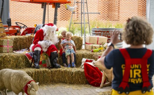 Santa poses with two children among hay bales, farm animals and Christmas gifts at the farmers’ market.