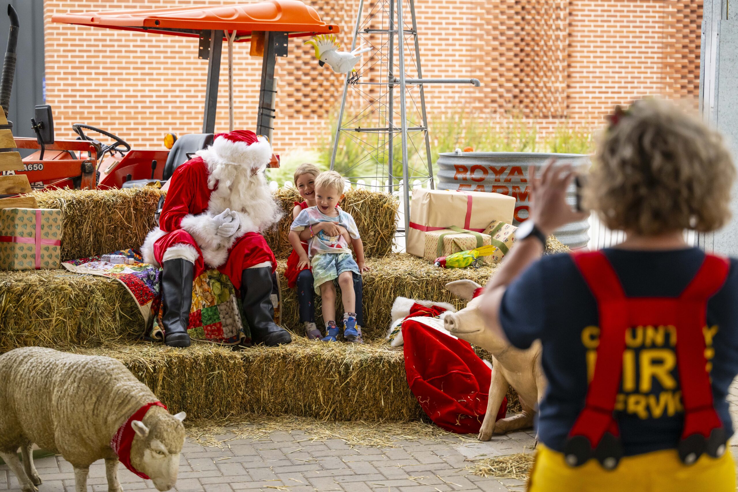 Santa poses with two children among hay bales, farm animals and Christmas gifts at the farmers’ market.