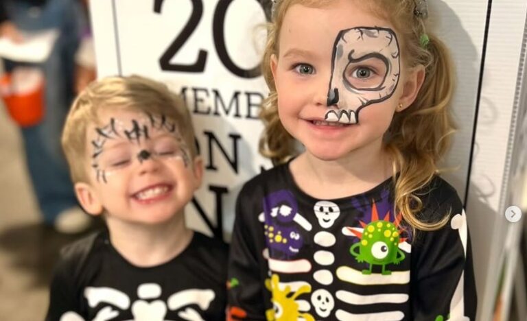 Two children in skeleton costumes smile at the Market, one with skull face paint and the other with spider face paint.
